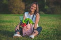 Beautiful vegan woman sitting on the grass with reusable bag with vegetables