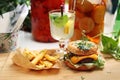 Vege cheeseburger, potato fries and lemonade on a wooden cutting board. Vegan lunch set. Plant-based meal.