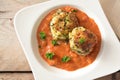 Vegetable balls from zucchini and potato in tomato sauce with parsley garnish in a modern white plate on a rustic wooden table, Royalty Free Stock Photo