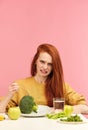 Vegetable diet. Sad dull woman holding broccoli on fork while making grimace