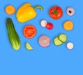 Vegetable mix on blue isolated background. Fresh yellow pepper, chopped tomatoes, onion, round cucumber slice, carrot, radish.