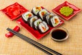 Vegetable rolls in plate, ginger, wasabi, sushi sticks, bowl with soy sauce on mat