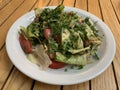 Vegetable salad of cucumbers, tomatoes and herbs on a white plate. Finely chopped vegetables in a salad bowl, on a wooden table. Royalty Free Stock Photo