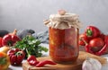 Vegetable salad with eggplant, carrot, peppers, onion and tomatoes in glass jar on wooden board, horizontal format. Closeup