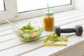 Vegetable salad and fruit smoothies and dumbbell lie on a white windowsill. Concept of healthy lifestyle physical Royalty Free Stock Photo