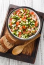 Vegetable salad with tomatoes, green peppers, onions and cucumbers close-up in a bowl on a wooden board. Vertical top view