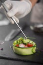 A vegetable snack made from fresh vegetables such as cucumber, tomato, feta cheese and microgreens. A gloved chef spreads green