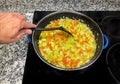 A vegetable stir fry with zucchini, onion and carrot a blue frying pan on a glass ceramic hob, and one hand with a black fork