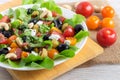 Greek vitamin fresh salad with tomatoes, olives, feta, salad leaves with cashews on a white plate.