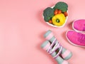 Vegetables capsicum, broccoli and tomato in heart shape plate, pink sneakers, pink dumbbells and measuring tape on pink