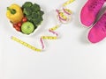 Vegetables capsicum, broccoli, tomatoes and apple in heart shape plate, pink sneakers or sport shoes, measuring tape on white