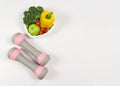 Vegetables capsicum, broccoli, tomatoes and green apple in heart shape plate and pink dumbbells on white background with copy