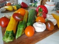 Vegetables on a cutting board on the kitchen table. Zucchini, tomatoes, champignons, peppers. Red, yellow, white, orange.