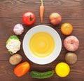 Vegetables and fruits lie around an empty plate on a wooden table.