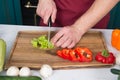 Vegetables getting cut on wooden cutting board. Hand slice green salad with ceramic knife. Hands cut vegetables with