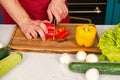 Vegetables getting cut on wooden cutting board. Hand slice pepper with ceramic knife. Food preparation and cooking