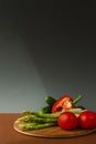 Vegetables lie on a wooden board: tomatoes, asparagus, cucumbers, red bell peppers. brown, dark gray background. place