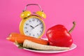 Vegetables on a plate and retro alarm clock isolated on pink background Royalty Free Stock Photo