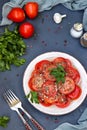 Vegetarian appetizer of tomatoes with garlic, parsley, dressed with honey and olive oil located in a plate on a dark background, Royalty Free Stock Photo