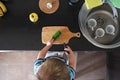 Vegetarian child cuts green cucumber with knife in kitchen, vegan kid helper, montessori training, top view above Royalty Free Stock Photo