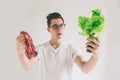 Vegetarian concept. Man offering a choice of meat or vegetables Salad leaves . Nerd is wearing glasses.