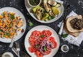 Vegetarian dinner table - quinoa and pumpkin salad, tomatoes, eggplants and peppers on the grill. On a dark background, top view.