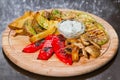 Vegetarian grill with zucchini, french fries, mushrooms, paprika, white sauce and dill on wooden plate