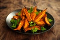 Vegetarian Oven baked sweet potato wedges, fries served on black plate with fresh parsley