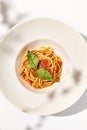 Vegetarian pasta with basil and tomatoes on white plate. Tomato pasta in summer menu with hard shadows Spaghetti with tomatoes on