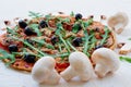 Vegetarian pizza with mushrooms, tomatoes, black olives, rucola on the white background decorated with fresh mushrooms Royalty Free Stock Photo