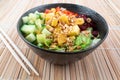 Vegetarian poke bowl in design black bowl with chopsticks below, on a reed pad background. Green cucumber, red pepper, peanuts, Royalty Free Stock Photo