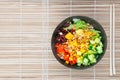 Vegetarian poke bowl in design black bowl with chopsticks below, on a reed pad background. Green cucumber, red pepper, peanuts, Royalty Free Stock Photo