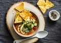 Vegetarian quinoa tomato soup with corn cheese chips, avocado and cilantro on grey background