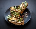 Wholemeal bread sandwiches with feta cheese, grilled zucchini, green asparagus, sugar peas, olive oil on a black plate Royalty Free Stock Photo