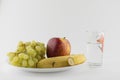 Vegetarian still life: red  ripe apples, bananas and seedless grapes on a white plate, close to the glass with pure water Royalty Free Stock Photo
