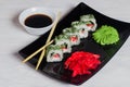 Vegetarian sushi rolls on a black square plate with wasabi, soy sauce and ginger. White wooden background Royalty Free Stock Photo