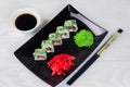 Vegetarian sushi rolls on a black square plate with wasabi, soy sauce and ginger. White wooden background Royalty Free Stock Photo