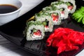 Vegetarian sushi rolls on a black square plate with wasabi, soy sauce and ginger. White wooden background Royalty Free Stock Photo