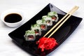 Vegetarian sushi rolls on a black square plate with wasabi, soy sauce and ginger. White wooden background Royalty Free Stock Photo