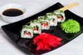 Vegetarian sushi rolls on a black square plate with wasabi, soy sauce and ginger. White wooden background Royalty Free Stock Photo