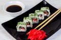 Vegetarian sushi rolls on a black square plate with wasabi, soy sauce and ginger. White wooden background Royalty Free Stock Photo