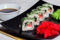 Vegetarian sushi rolls on a black square plate with wasabi, soy sauce and ginger. White wooden background Royalty Free Stock Photo