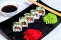 Vegetarian sushi rolls on a black square plate with wasabi, soy sauce and ginger. White wooden background Royalty Free Stock Photo