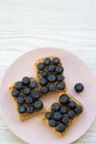 Vegetarian toasts with peanut butter, blueberries and chia seeds on a pink plate over white wooden surface, top view. Healthy eati Royalty Free Stock Photo