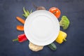Vegetarian vegan cousine concept with empty plate and vegetables in background on black surface Royalty Free Stock Photo