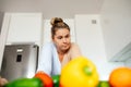 Vegetarianism. Young woman at home in white modern kitchen is thinking and looking at fresh juicy vegetables.