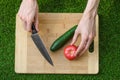 Vegetarians and cooking on the nature of the theme: human hand holding cucumber, tomato on a cutting board and a background of gre