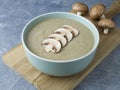 Veggie mushroom cream soup with raw mushroom slices in the blue bowl on wooden cutting board
