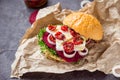 Vegitarian burger with beet slices, microgreen sprouts, tofu cheese, dried tomatoes and onion on kraft package paper on dark stone