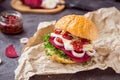 Vegitarian burger with beet slices, microgreen sprouts, tofu cheese, dried tomatoes and onion on kraft package paper on dark stone